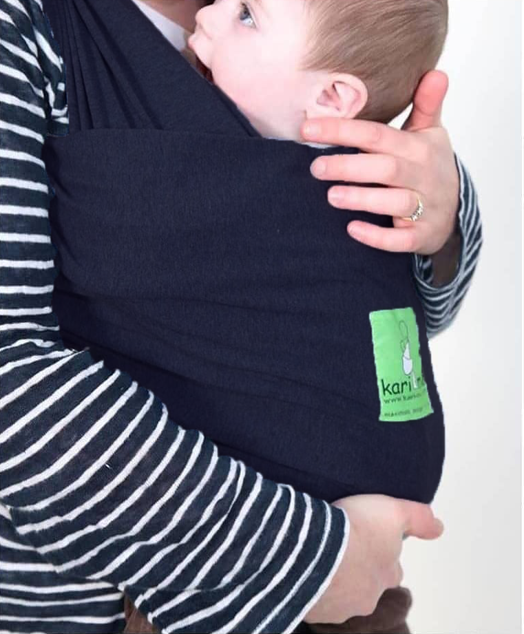 Person holding a baby in a navy blue carrier with a visible brand logo on a white background